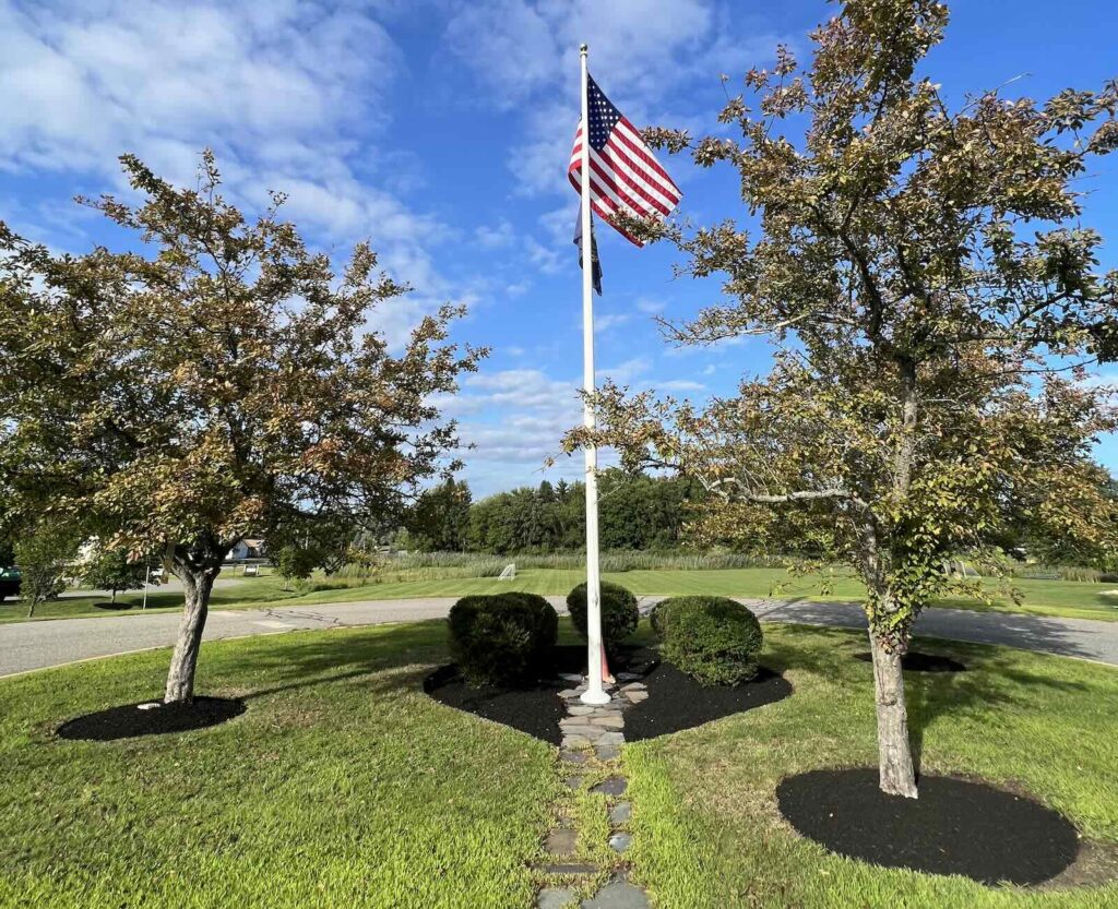 Freshly landscaped garden beds with mulch and trimmed shrubs around flagpole in Greenland NH